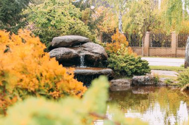 Bahçe manzaralı bir sonbahar bahçesinde taşlardan ve çiçeklerden oluşan yapay şelale.