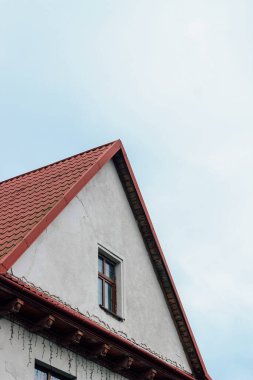Gri bulutlu gökyüzünün arka planında pencereleri olan modern bir evin turuncu çatısı