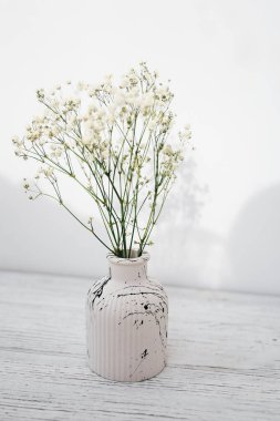 Zarif, beyaz bir vazo, narin çiçekler, parlak bir ışıkla ahşap yüzeyde dizilmiş.