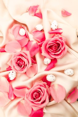 Güzel pembe güller ve yumuşak kumaş arkaplanda sıralanmış narin yumurtalar.
