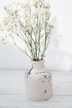 Zarif, beyaz bir vazo, narin çiçekler, parlak bir ışıkla ahşap yüzeyde dizilmiş.