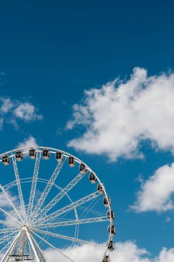 Beyaz bulutlar açık mavi gökyüzünde sürüklenirken ziyaretçiler dönme dolabın keyfini çıkarıyorlar..