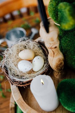 Yeşillik ve yanan bir mum ile çevrili doğal bir yuvada dekoratif yumurtalar huzurlu bir bahar ortamı yaratır..