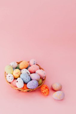 Paskalya kutlaması için pembe arka planda bir sepete yerleştirilmiş dekoratif renkli yumurtalar.