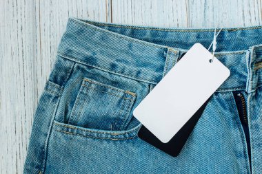 Üzerinde fiyat etiketi olan kot pantolonlar, sıradan tarzlarını ve ekonomik durumlarını vurgulayan, ahşap bir yüzeyde yatıyor..