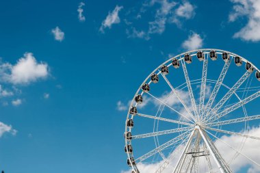 Beyaz bulutlu açık mavi gökyüzüne karşı büyük bir dönme dolap kulesi. Güneşli bir gün, gezinin tadını çıkarmak için ziyaretçileri cezbediyor..
