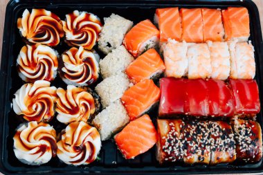 Suşi rulolarının renkli bir çeşidi somon, yengeç ve yaratıcı garnitürleri siyah bir tepside sergiliyor..