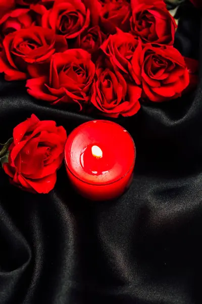 Canlı kırmızı güller ve mum koyu renk kumaş üzerinde romantik bir ortam yaratır.