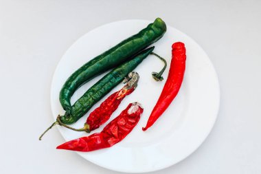 Yeşil ve kırmızı biberlerden oluşan bir koleksiyon, canlı renklerini ve yemek pişirmek için eşsiz şekillerini gösteren beyaz bir tabakta sergileniyor..