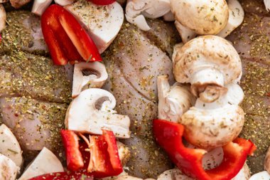 Baharatlı tavuğun etrafına kırmızı dolma biber ve mantar da dahil olmak üzere çeşitli taze sebzeler dizilir..