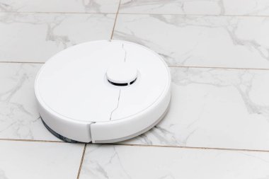 Robot bir elektrikli süpürge modern bir oturma odasında mermer zeminde tozları ve enkazı verimli bir şekilde temizlerken hareket eder..