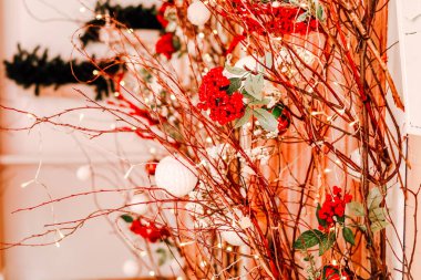 Parlak kırmızı çiçekler ve beyaz süslemeler ince dallar ve sicim ışıklarıyla iç içe geçerek tatil toplantıları için mükemmel bir şenlik ortamı yaratıyor..