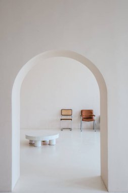 Parlak iç mekan, minimalist mobilyalara giden kemerli bir yol gösteriyor. Düşük masa ve basit sandalyeler, sakin bir atmosfer yaratıyor..