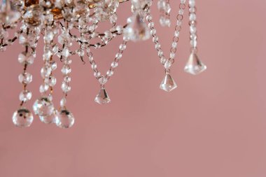 Işıldayan kristallerle süslenmiş karmaşık bir avize tasarımı odayı aydınlatan pastel pembe bir zemin..