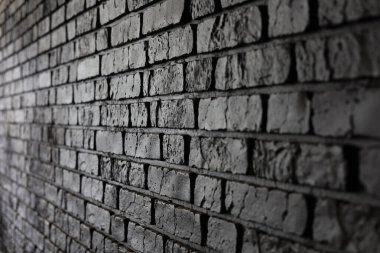 Siyah tuğla bir duvarın detaylı bir görüntüsü, tuğlalar arasındaki pürüzlü yüzeyleri ve çizgileri vurgulayan dokuyu ve gölgeleri gösterir..