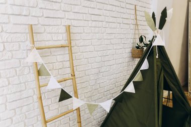 Kapalı bir alanda üçgen çelenklerle süslenmiş yeşil bir çadır var..