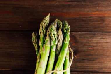 Birbirine bağlanmış taze kuşkonmaz demetleri, canlı yeşil renklerini ve doğal dokularını sergileyen kaba ahşap bir yüzeyde otururlar..