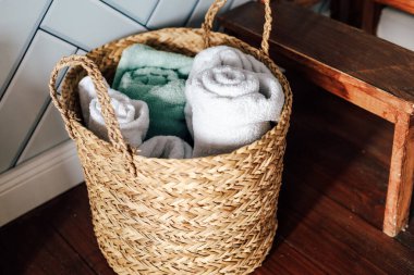 Dokuma sepet yumuşak rulo havlularla doludur gri ve yeşil tonlarda sıcak bir davet odasına yerleştirilmiş ahşap mobilyalarla..