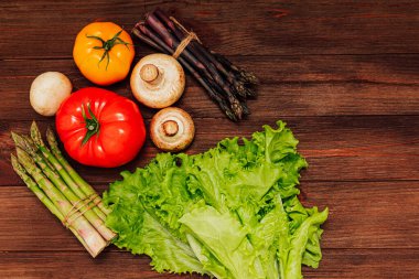 Domates, kuşkonmaz ve mantarlar da dahil olmak üzere parlak ve taze sebzeler ahşap bir masada yemek pişirmek için idealdir..