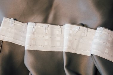 Dokulu kumaş, yumuşak bir yüzeyde, işçilik ve tasarımın ön plana çıkarıldığı tarafsız bir gölgede karmaşık bir şekilde dikilmiş elastik bandı gösteriyor..