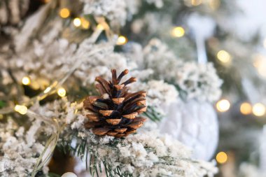 Güzel dekore edilmiş bir Noel ağacı suni karın ortasında doğal bir çam kozalağı sergiliyor ve sıcak ışıklar yanıp sönerek rahat bir atmosfer yaratıyor..