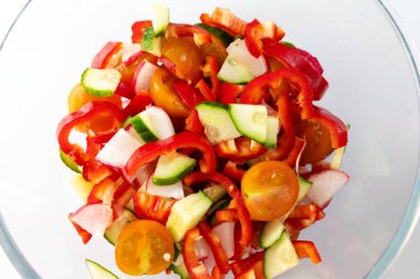 Doğranmış salatalıklar, kırmızı dolmalık biberler ve kiraz domatesleri sağlıklı bir salatayı gösteren cam bir kasede karıştırılır..