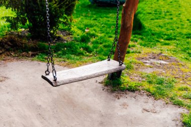 Tahtadan yapılmış tek bir salıncak, gür yeşil çimen ve yeşilliklerle dolu canlı bir parktaki sağlam bir ağaçta asılı duruyor..