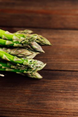 Canlı yeşil kuşkonmaz mızrakları, sade bir ahşap yüzey üzerinde, sağlıklı yemekler için mükemmel bir şekilde bir araya getirilir..