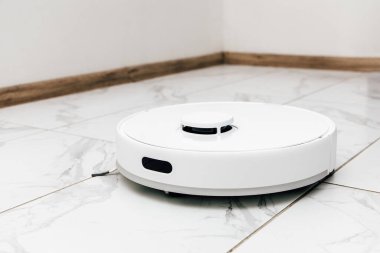 Robotik bir elektrikli süpürge, çağdaş bir yaşam alanındaki temiz fayanslı zeminde hareket halinde akıllı ev teknolojisi sergiliyor..