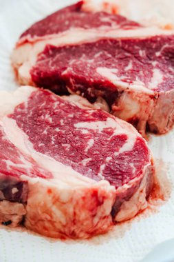 İki çiğ pirzola bir kağıt havlunun üzerinde mermer sergileniyor ve pişirmeye hazır. Barbekü ya da biftek gecesi için ideal..