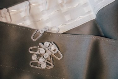 Küçük temiz plastik klipsler beyaz malzemelerin yanındaki gri kumaş üzerinde duruyor. Yaratıcı bir çalışma alanında dikiş projesinin devam ettiğini gösteriyor..