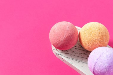 Pembe turuncu ve mor tonlarda üç canlı banyo bombası canlı pembe bir arka planla mermer bir tepside sergilenir..