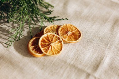 İnce dilimler halinde kurutulmuş narenciye, bej bir keten kumaşın üzerine serilmiş taze yeşil yapraklar kırsal ve organik bir his yaratıyor..