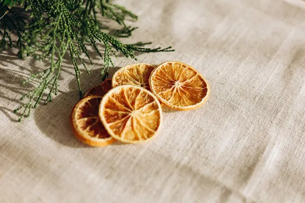İnce dilimler halinde kurutulmuş narenciye, bej bir keten kumaşın üzerine serilmiş taze yeşil yapraklar kırsal ve organik bir his yaratıyor..