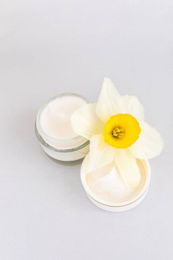 Süsleme için sarı ve beyaz bir çiçek eşliğinde pürüzsüz bir yüzeye iki küçük kremalı cilt ürünleri yerleştirilir..
