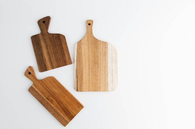 Değişen şekil ve tonlarda üç farklı tahta kesme tahtası zarif bir şekilde parlak beyaz bir arka plana yerleştiriliyor ve dokularını sergiliyorlar..