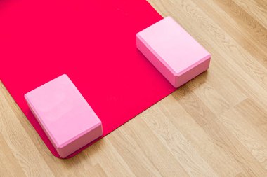Parlak stüdyo, yoga seansı için ayarlanmış kırmızı yoga minderi ve iki pembe blok içeriyor. Antrenman için sakin bir ortam yaratıyor..