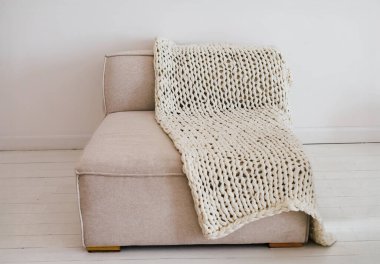 Şık bir kanepe, minimalist bir odada sıcak bir atmosfer yaratan örgü örülmüş bir battaniyeyle süslenir. Doğal ışık samimi sahneyi vurgular.