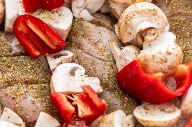 Terbiye edilmiş tavuk parçaları baharatlı ve ızgaradan önce dilimlenmiş kırmızı dolma biber ve mantarla karıştırılır..