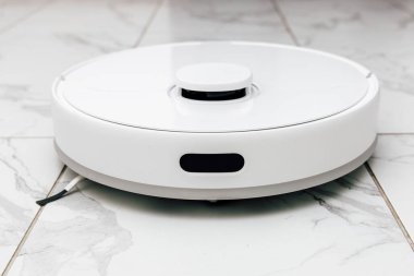 Gösterişli, beyaz bir robot elektrikli süpürge şık bir evde parlak fayanslı bir zeminde oturur. Verimli temizlik ve rahatlık için tasarlanmıştır..