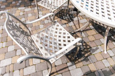 Karmaşık tasarımları olan metal bir sandalye ve uyumlu bir masa güneşli bir kaldırım taşından verandada oturup rahatlamaya ve eğlenmeye davet ediyor..