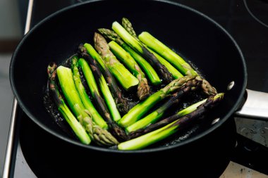 Parlak yeşil kuşkonmaz mızrakları sobanın üstünde sotelenmiş siyah tavada canlı bir pişirme süreci sergiliyor..