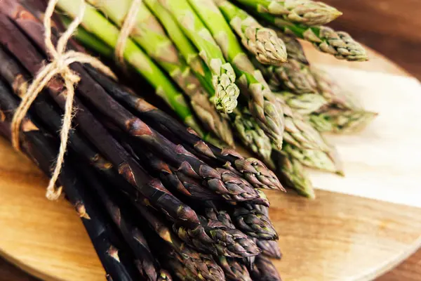 Yeşil ve mor kuşkonmaz demetleri ahşap bir kesme tahtasına bağlanmış taze kalitelerini ve canlı renklerini sergiliyorlar..