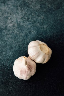 Mutfak ortamında koyu dokulu bir yüzeye doğal güzelliklerini ve dokularını sergileyen iki taze sarımsak karanfili yerleştirilir..