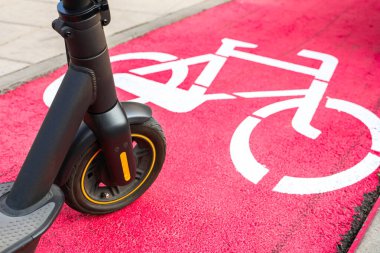 Elektrikli scooter, şehir parkında parlak kırmızı bir bisiklet yolunda duruyor..