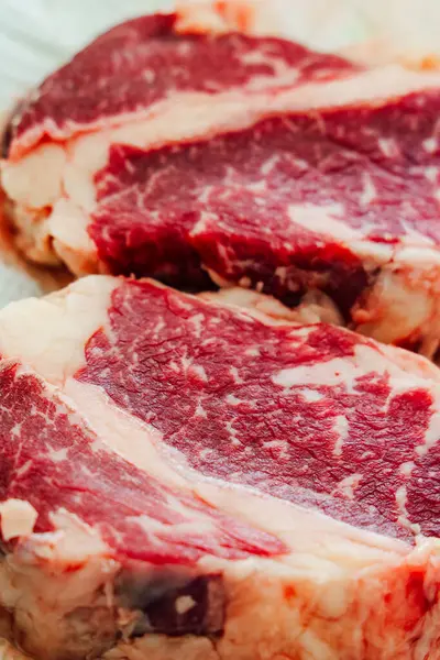 İki taze mermer biftek, zengin renklerini ve kalitelerini gösteren ahşap bir tahtanın üzerinde oturur. Izgara ya da kızartma için ideal..