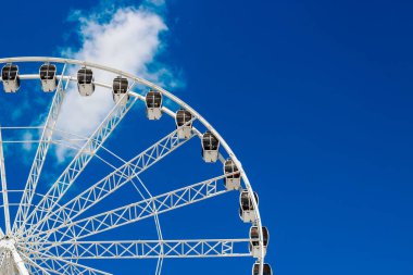 Dönme dolap bir lunaparkta dimdik duruyor. Kabarık bulutlu, çarpıcı mavi gökyüzüne karşı birden fazla yolcu kabini sergiliyor..