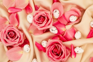 Güzel pembe güller narin taç yaprakları ve yumuşak bir perde üzerinde küçük dekoratif yumurtalarla düzenlenir ve davetkar bir bahar atmosferi yaratır..