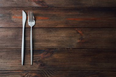 Gümüş bıçak ve çatal, basit ve zarif bir yemek deneyimi için kahverengi ahşap bir masaya güzelce yerleştirilir..