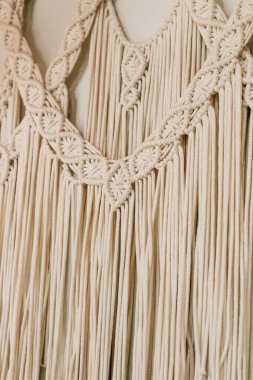 Ayrıntılı bir makrome duvar asılı yumuşak bej rengi ve zarif dokuları gösteren çeşitli düğüm teknikleri ve desenleri içerir..